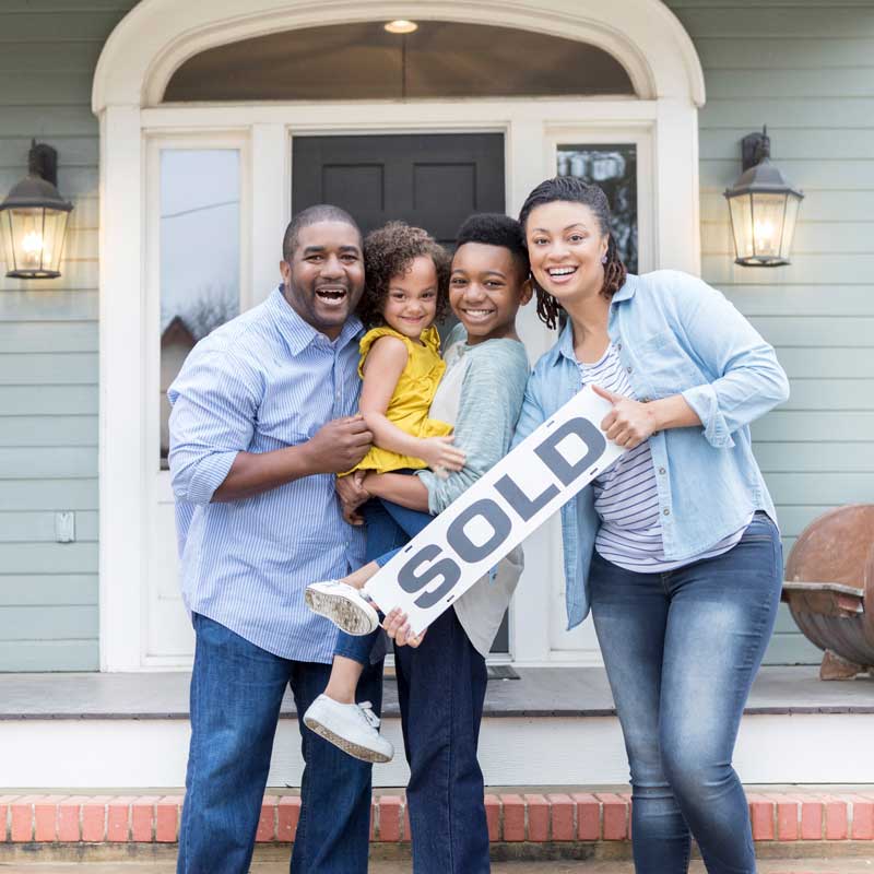Happy family of four holding Sold sign in front of door
